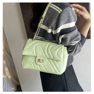 Detail of mint green quilted chain bag with gold twist lock on a striped sweater