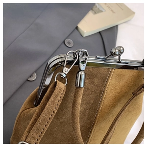 Detail of tan suede shell bag with metal clasp and thin shoulder strap for women
