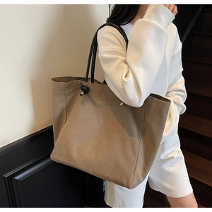 Detail of a large khaki suede tote bag with slim black handles and silver hardware