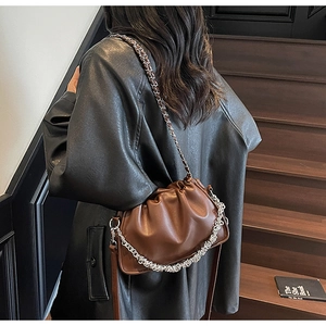 Brown leather pleated dumpling bag with silver chain detail worn by model in street style