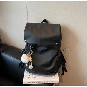Detailed side view of black nylon backpack showing mesh pocket and fluffy ball charm