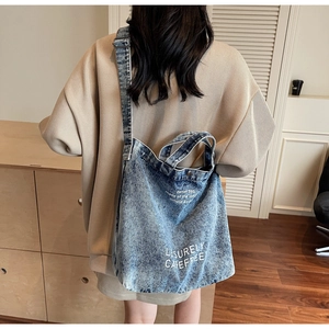 Blue washed denim tote bag with white text print shown on model in a casual setting