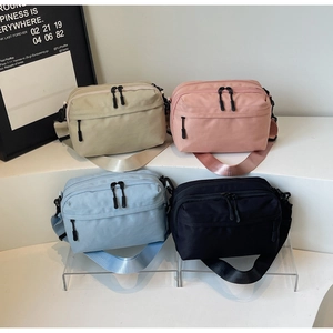 Close-up of multi-pocket nylon crossbody bags in four colors on a tiered display