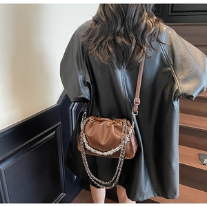 Detail of a brown pleated cloud bag with silver chain strap worn over a black leather jacket