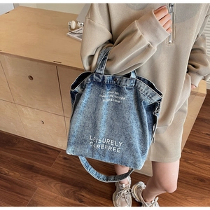 Detail of blue denim tote bag featuring white graphic print and adjustable shoulder straps