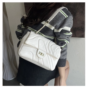Detail view of a white quilted shoulder bag with gold chain and twist lock on a model