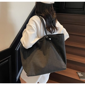 Detail of black canvas tote bag with silver knob and fine shoulder strap on model