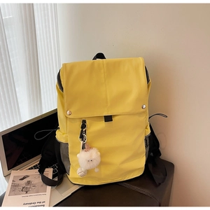Detail of yellow nylon backpack with magnetic flap and white plush charm accessory