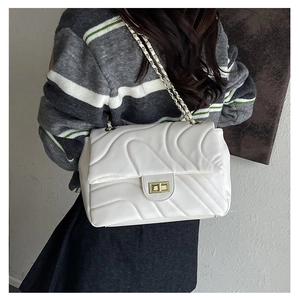 Close-up of white quilted chain bag with gold twist lock on a casual outfit
