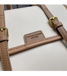 Detail view of cream-colored tote bag with brown leather strap and gold-tone buckle