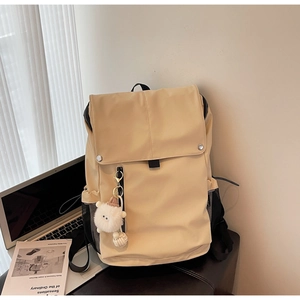 Detail of beige nylon backpack with large flap, silver metal buckle and plush pendant