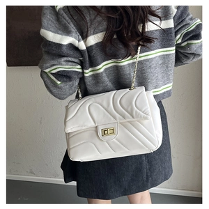 Detail of white quilted underarm bag with gold chain strap and elegant wave pattern texture