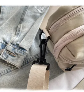 Detail of durable black plastic swivel hook and wide nylon strap on beige crossbody bag