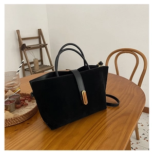 Close-up of matte black suede tote bag with gold metal buckle on a wooden table