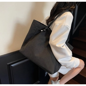 Detail view of large black canvas tote bag with silver metal buckles and knot accents