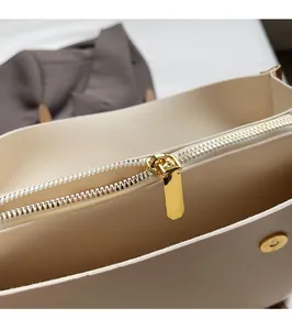Detailed close-up of golden metal zipper and magnetic buckle on beige leather tote bag