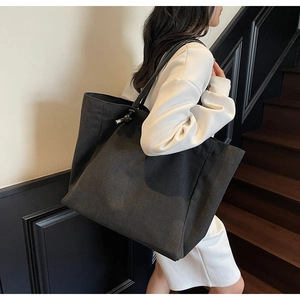 Side view of large black canvas tote bag with leather straps and silver hardware detail