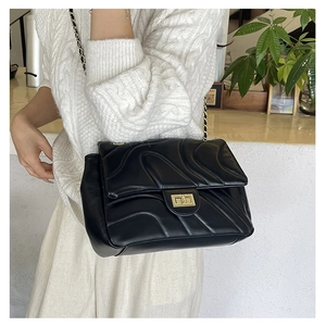 Detail of wavy quilted black leather bag with gold twist lock and woven chain strap