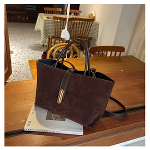 Detail of vintage brown suede tote bag with leather straps and gold metal clasp on table