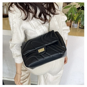 Quilted black chain crossbody bag with wave stitching and gold turn-lock closure on model