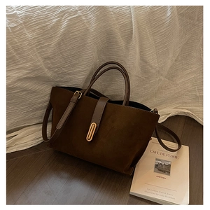 Detail of vintage matte brown tote bag with gold metal buckle on white fabric background