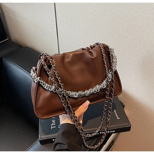 Detail of dark brown leather cloud bag with silver metal chains and pleated texture