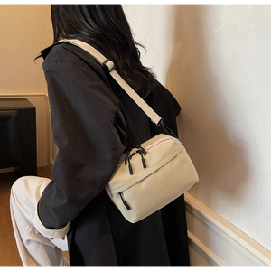 Detail view of beige canvas crossbody bag with black double zippers and wide shoulder strap