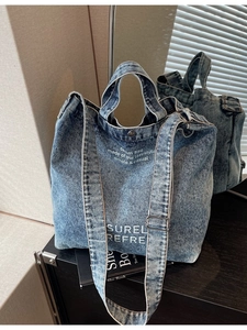 Blue washed denim tote bag with white text print, adjustable strap and metal buckle