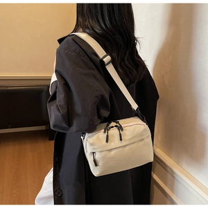 Close-up of minimalist beige crossbody bag with premium black zipper and wide shoulder strap