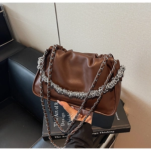 Close-up of a dark brown ruched dumpling bag with silver chain straps on a black book
