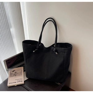Minimalist black canvas tote bag with knot detail and slim handles in office setting