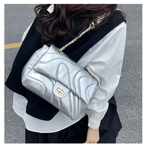 Detailed view of silver quilted crossbody bag with gold chain strap worn by a model