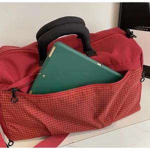 Close-up of wine red travel bag front zipper pocket holding a green tablet for size