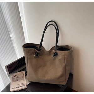 Detail of khaki canvas tote with black leather knotted shoulder strap on office desk