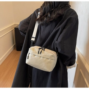 Detail of a minimalist off-white nylon crossbody bag showing the zipper and adjustable strap