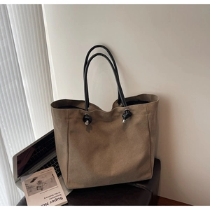 Close-up of a large khaki tote bag with black leather straps and silver metal knot details