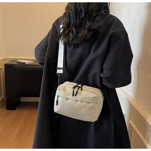 Detail view of the cream crossbody camera bag with wide strap on a dark winter coat