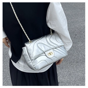Detail of silver wavy quilted texture and gold turn-lock closure on chain crossbody bag