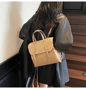 Rear view of a light camel leather backpack featuring gold hardware on a wooden staircase