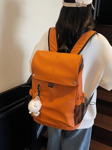 Large orange nylon backpack for women featuring flap closure and plush charm accessory