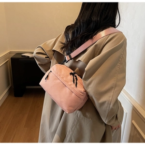 Detail view of a pink nylon crossbody bag with dual black zippers on a female model
