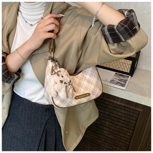 Detail of cream checkered crescent bag with brown strap and plush sheep charm accessory