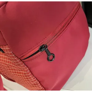 Detail of smooth black circular zipper and white grid mesh pocket on the maroon travel bag