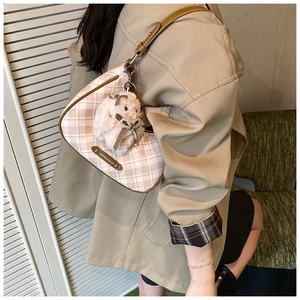 Close-up of pink checkered saddle bag with white plush lamb charm and leather strap