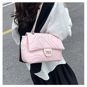Detail view of pink quilted crossbody bag with gold chain strap worn by a model outdoors