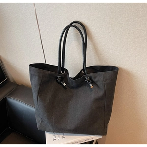 Detail of black canvas tote bag showing knotted tube handles and metallic hardware ends
