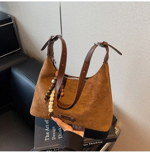 Détail macro du sac bandoulière en daim marron foncé avec perles en bois et logo métal