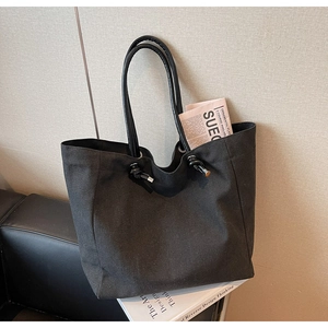 Detail of black canvas tote bag with decorative drawstring knot and leather handle