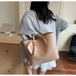 Detail of khaki leather tote with houndstooth scarf on a model in a modern office