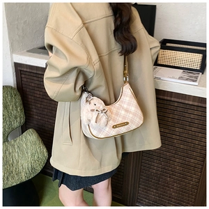 Detail of checkered canvas tote bag with brown leather strap and plush charm on model